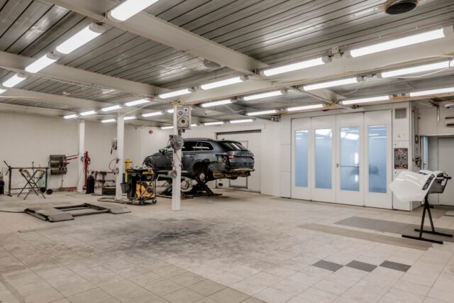 Interiorul unui service auto mic și ordonat, cu o mașină ridicată pe elevator și scule pe perete
