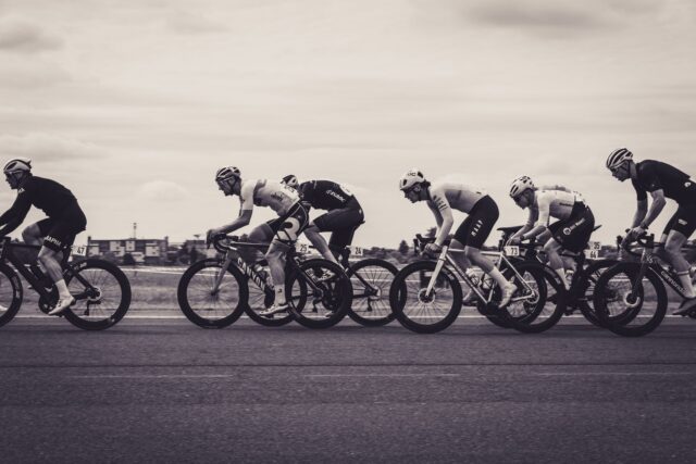 Grup de cicliști amatori care pedalează pe o șosea de țară, în timpul unei curse de lungă distanță