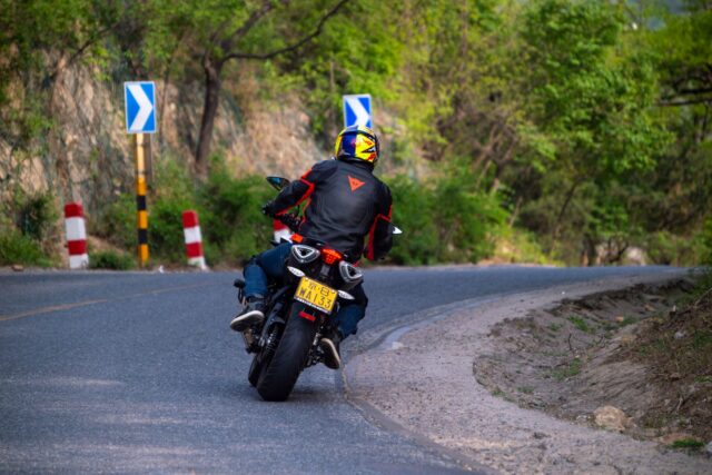 Motociclist echipat complet, cu cască integrală și geacă de protecție, pe un drum de țară