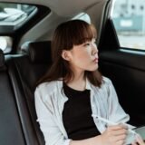 Pasager care privește drumul pe geamul mașinii, cu geamul ușor coborât, în timpul unei călătorii